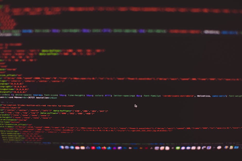 A person working on a laptop with a black keyboard and a bright, high-resolution screen displaying lines of colorful code in green, blue, and white against a dark background. The workspace appears to 